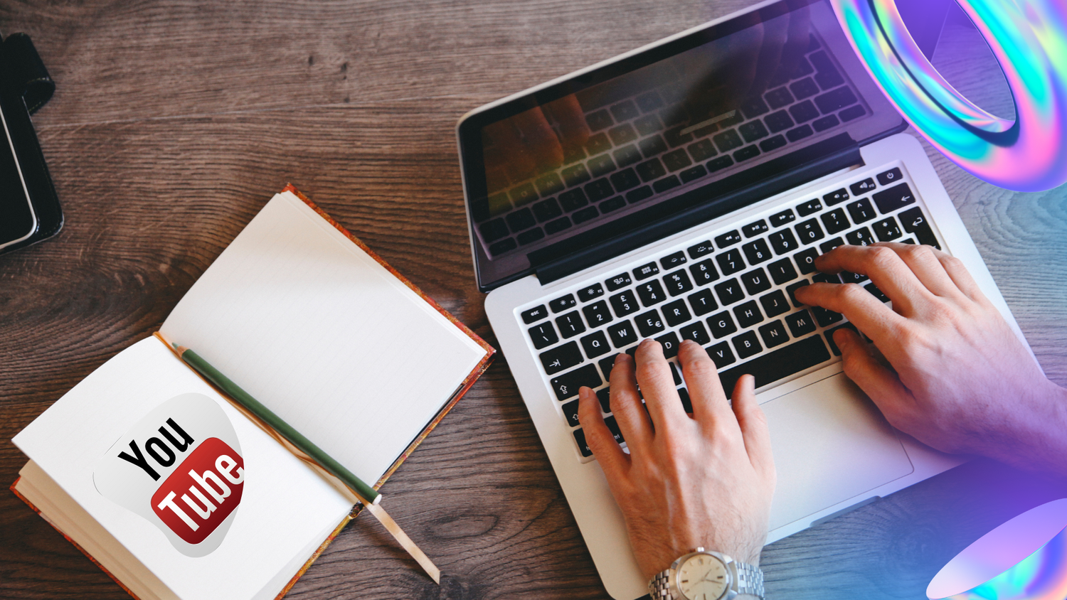 Overhead view of hands typing on a laptop next to an open notebook bearing a YouTube logo sticker